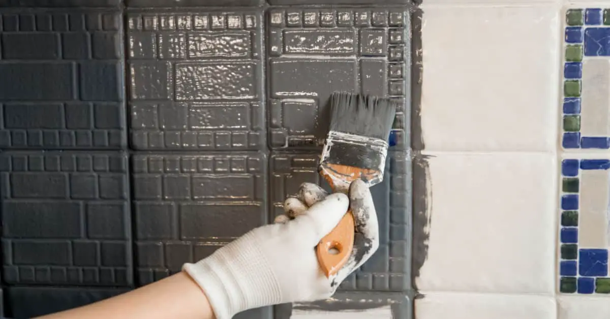 Gros plan sur une main en gant blanc peignant le carrelage mural en gris à l’aide d’un pinceau
