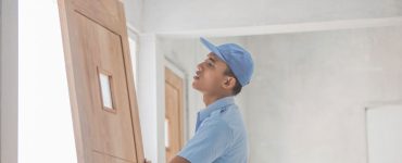 Un homme en casquette bleue installant une porte en bois