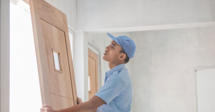 Un homme en casquette bleue installant une porte en bois