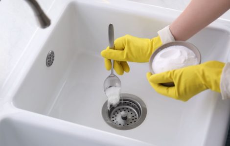 Une femme en gants jaunes verse une poudre blanche dans l'évier
