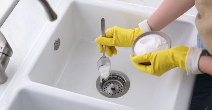 Une femme en gants jaunes verse une poudre blanche dans l'évier