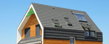 Une maison avec des bardages en bois et un toit noir avec des panneaux solaires