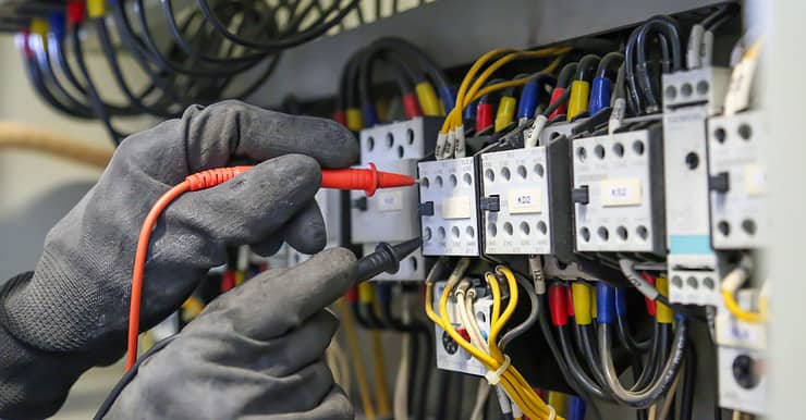 Zoom sur les mains d’un électricien qui vérifie la tension du courant électrique sur le tableau électrique