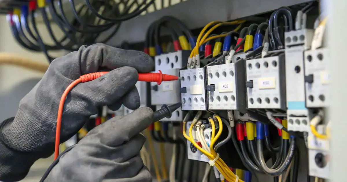 Zoom sur les mains d’un électricien qui vérifie la tension du courant électrique sur le tableau électrique