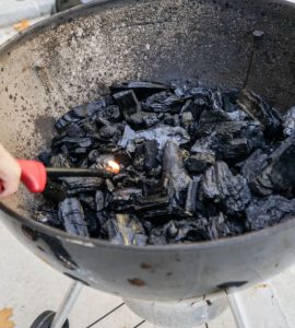 Une personne allumant le feu dans un gril à charbon à l'aide d'un briquet