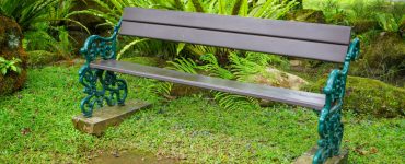 Une longue chaise en bois, avec cadre en fer dans un jardin