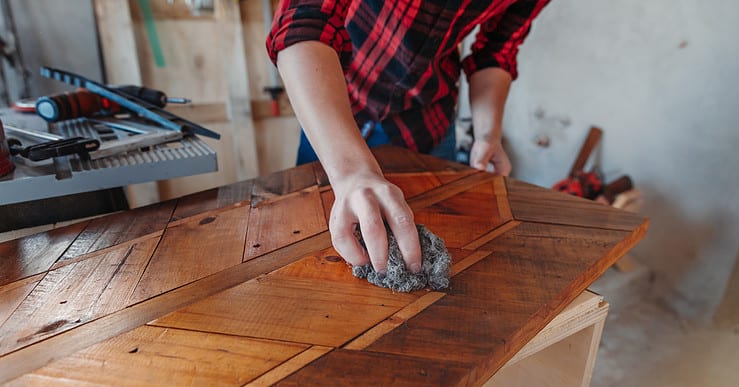 Un homme en train de cirer un meuble en bois dans son atelier