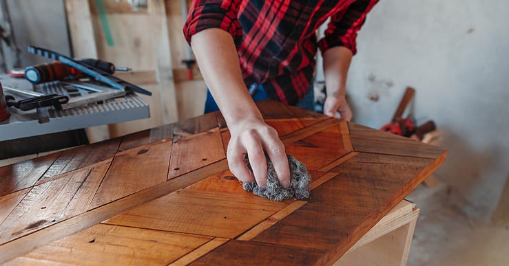 Un homme en train de cirer un meuble en bois dans son atelier