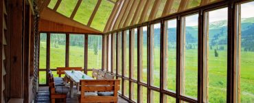 Une longue table à manger placée dans une véranda avec une vue sur le paysage de verdure