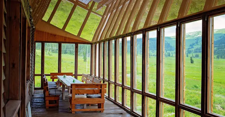 Une longue table à manger placée dans une véranda avec une vue sur le paysage de verdure