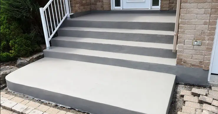 Un escalier en béton rénové devant la porte principale d’une maison