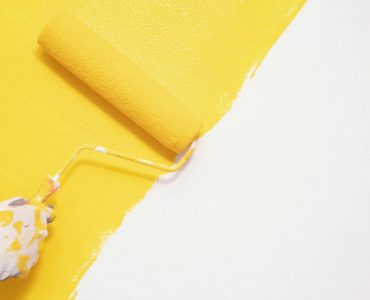 Zoom sur une main en gant en train de peindre un mur en jaune