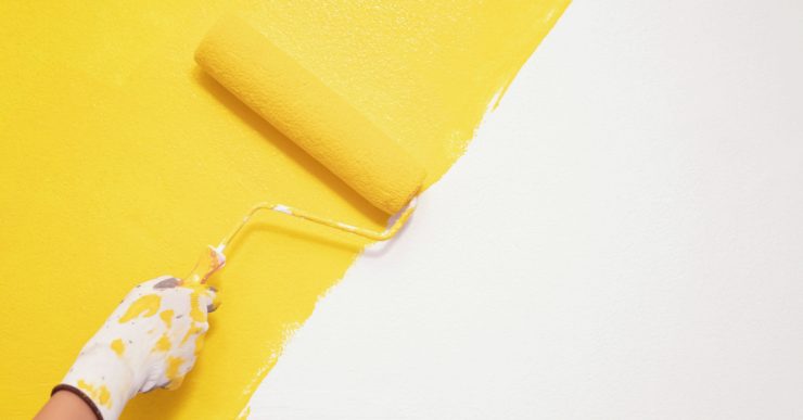 Zoom sur une main en gant en train de peindre un mur en jaune