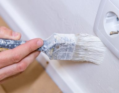 Main d'un homme avec un pinceau en train de peindre le mur en blanc