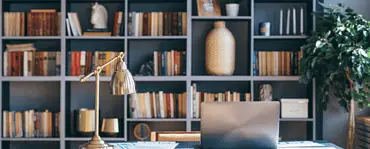 Un ordinateur portable posé sur un bureau bleu, avec une bibliothèque en fond