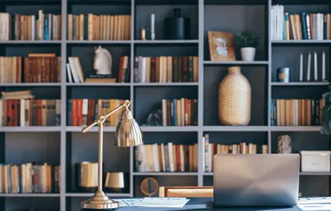 Un ordinateur portable posé sur un bureau bleu, avec une bibliothèque en fond