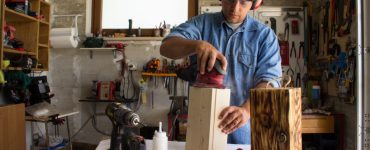 Un homme portant un casque antibruit en train de poncer un caisson en bois dans un atelier