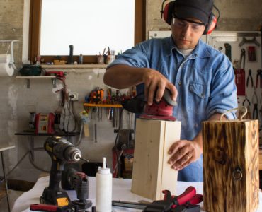 Un homme portant un casque antibruit en train de poncer un caisson en bois dans un atelier