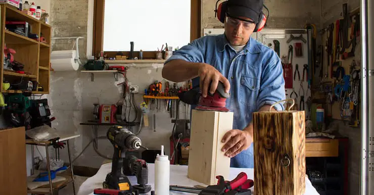 Un homme portant un casque antibruit en train de poncer un caisson en bois dans un atelier