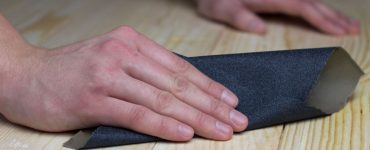 Zoom sur les mains d’un homme en train de poncer une surface en bois avec du papier abrasif
