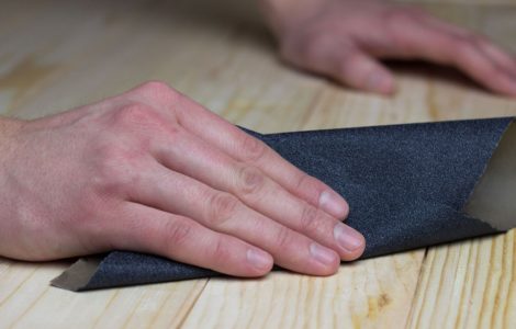 Zoom sur les mains d’un homme en train de poncer une surface en bois avec du papier abrasif