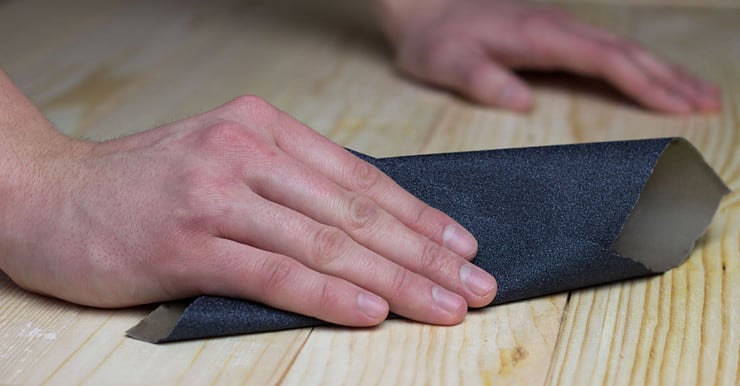 Zoom sur les mains d’un homme en train de poncer une surface en bois avec du papier abrasif
