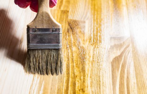 Gros plan sur la main d’une personne appliquant du vernis sur du bois à l’aide d’un pinceau