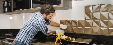 Un homme pose un carrelage mural dans la cuisine