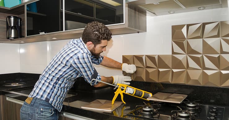 Un homme pose un carrelage mural dans la cuisine