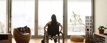 Une femme en fauteuil roulant dans une chambre avec baies vitrées