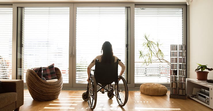 Une femme en fauteuil roulant dans une chambre avec baies vitrées