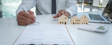 Un homme en cravate signe un contrat, avec des maquetes de maison sur la table