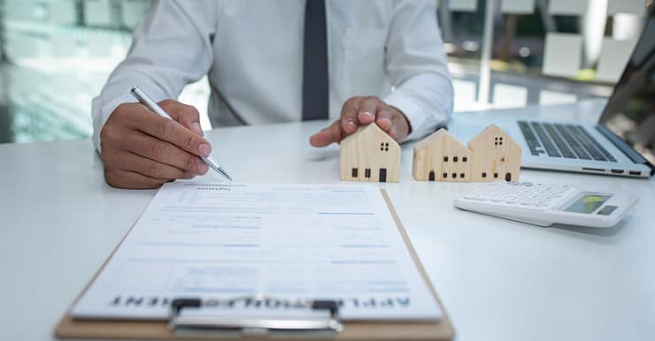 Un homme en cravate signe un contrat, avec des maquetes de maison sur la table