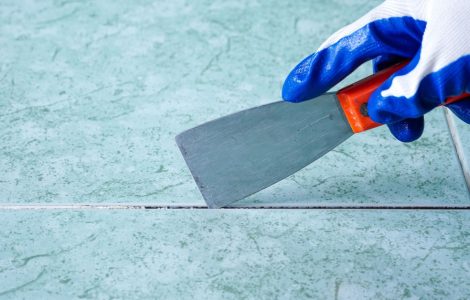 Un homme avec une spatule en train d'enlever les joints du carreau