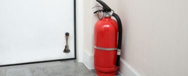 Un extincteur rouge posé au sol, au coin du mur, près d'une porte blanche