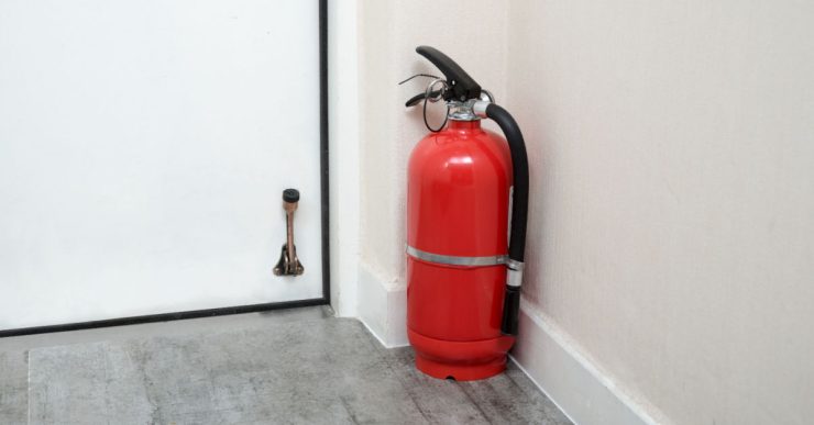 Un extincteur rouge posé au sol, au coin du mur, près d'une porte blanche