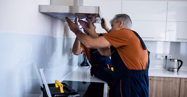 Deux hommes en combinaison installant un extracteur de cuisine