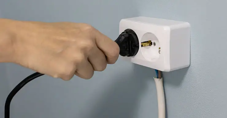 Zoom sur la main d'une personne mettant un cordon d'alimentation dans une prise électrique