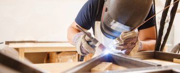 Un homme portant un masuqe réalise une soudure à l'arc dans son atelier