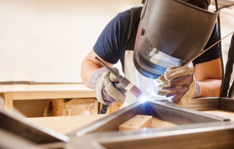 Un homme portant un masuqe réalise une soudure à l'arc dans son atelier
