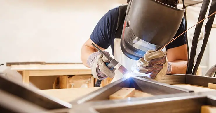 Un homme portant un masuqe réalise une soudure à l'arc dans son atelier