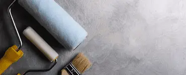 Des rouleaux de peinture et un pinceau posés sur un sol gris
