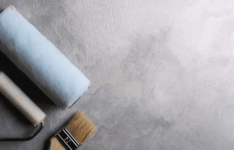 Des rouleaux de peinture et un pinceau posés sur un sol gris