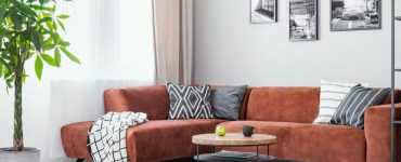 Un salon avec un canapé d’angle marron, une table basse ronde en bois et un tapis gris