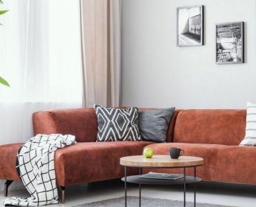 Un salon avec un canapé d’angle marron, une table basse ronde en bois et un tapis gris