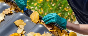 Zoom sur un homme en gants bleus enlevant les feuilles mortes sur une gouttière