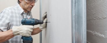 Un homme utilise une visseuse électrique sans fil pour fixer des plaques de plâtre sur le mur