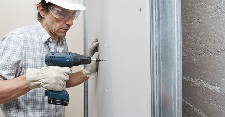 Un homme utilise une visseuse électrique sans fil pour fixer des plaques de plâtre sur le mur