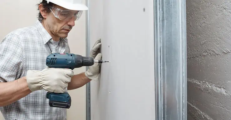 Un homme utilise une visseuse électrique sans fil pour fixer des plaques de plâtre sur le mur