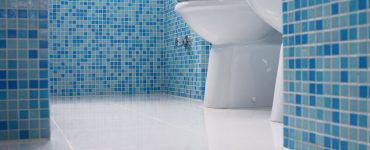 Vue sur les toilettes d’une salle de bain avec des murs en mosaïques bleus